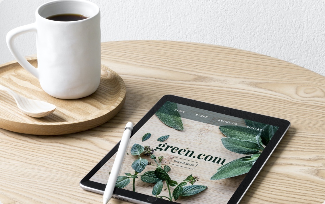 Una taza de café sobre una mesa. Al lado, una tableta que muestra un ejemplo de una página web de jardinería creada con Jimdo.